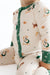 A close-up of a baby wearing a long-sleeve zip-front onesie and matching pants in cream with green trim and a dog football print, seated against a white background.