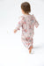 A baby wearing a light pink long-sleeve footless sleeper with a red and blue floral print, shown from behind as they walk barefoot on a white background.