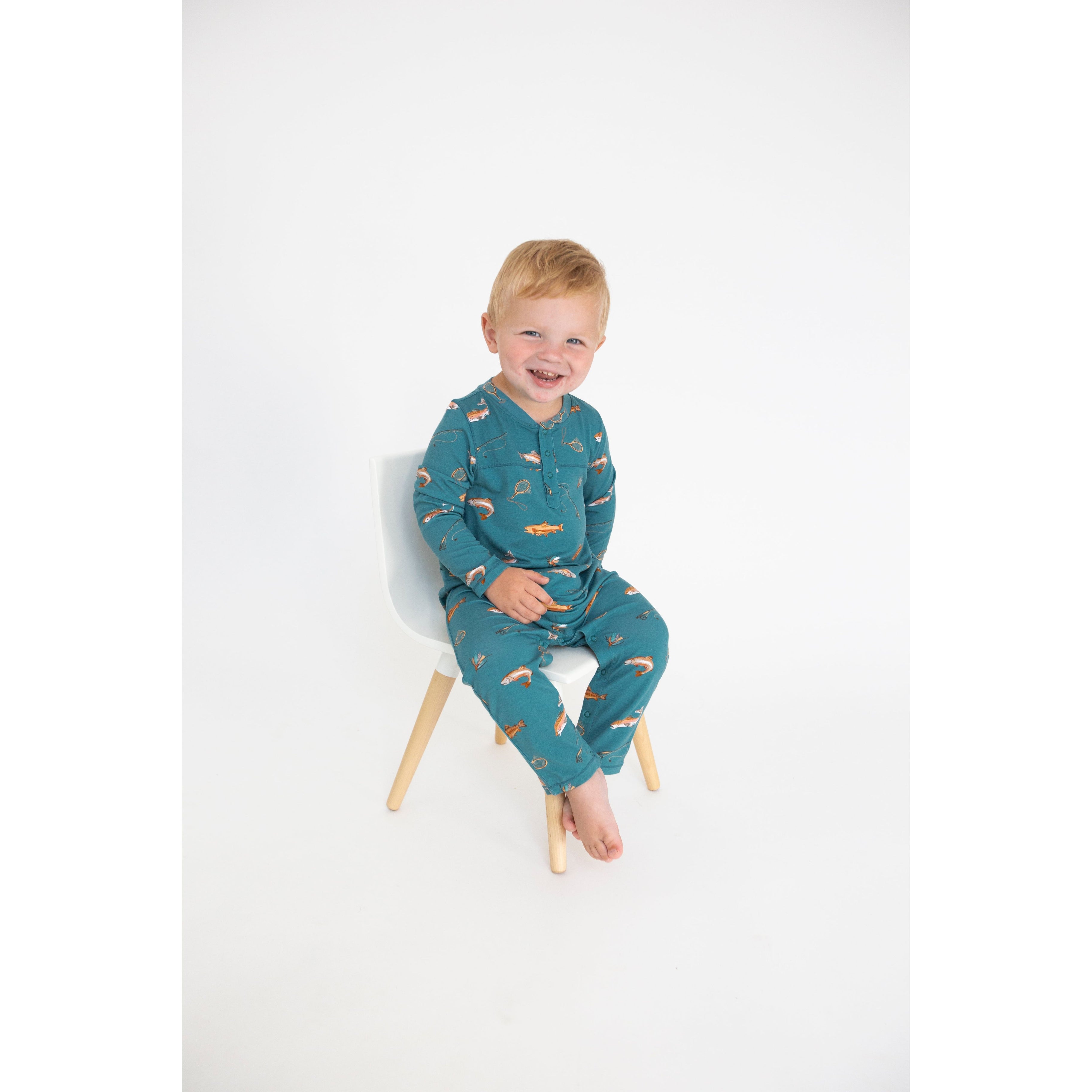 toddler boy wearing teal long sleeve romper with pockets and 3 snaps with brown trout print
