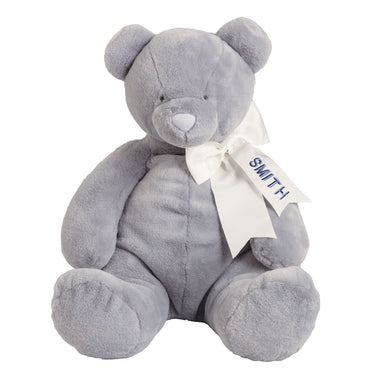 Gray teddy bear with a white bow and monogram tag on a white background
