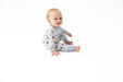 A baby sitting on a white studio background wearing a light blue long-sleeve pajama romper with a small football print.