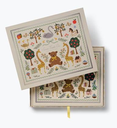 Illustrated keepsake baby book by Rifle Paper Co. with a cream cover featuring a teddy bear giraffes swan flowers trees and colorful nursery motifs