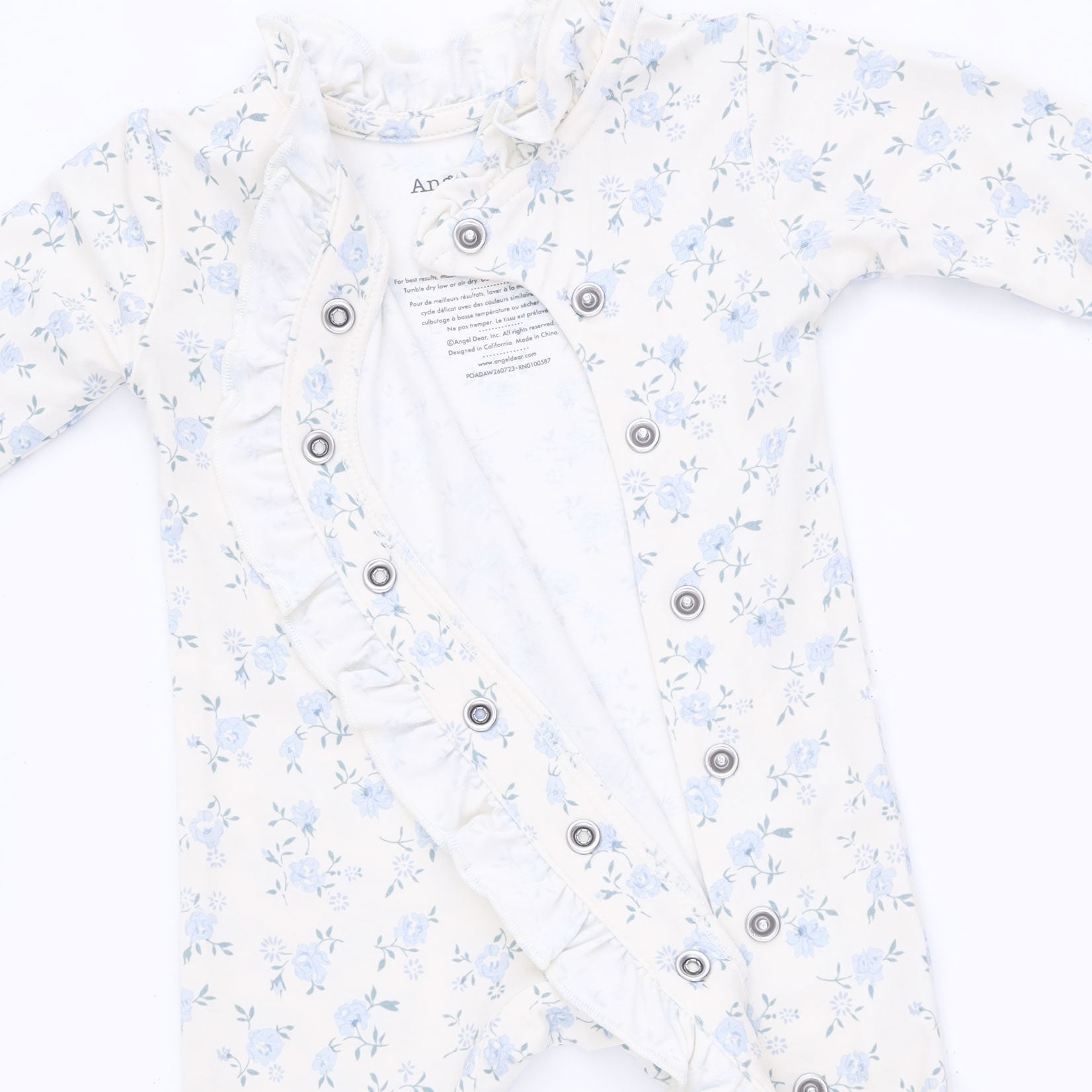 A baby long-sleeve romper in white with a light blue floral print, featuring ruffled trim along the neckline and front button closure.