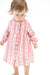A toddler girl wearing a pink and white striped long-sleeve dress with a ruffled collar and button front, standing against a plain white background.