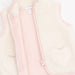 A close-up of a children's zip-front vest with a soft cream sherpa fleece exterior, light pink lining and trim, and a heart-shaped patch on the front pocket.