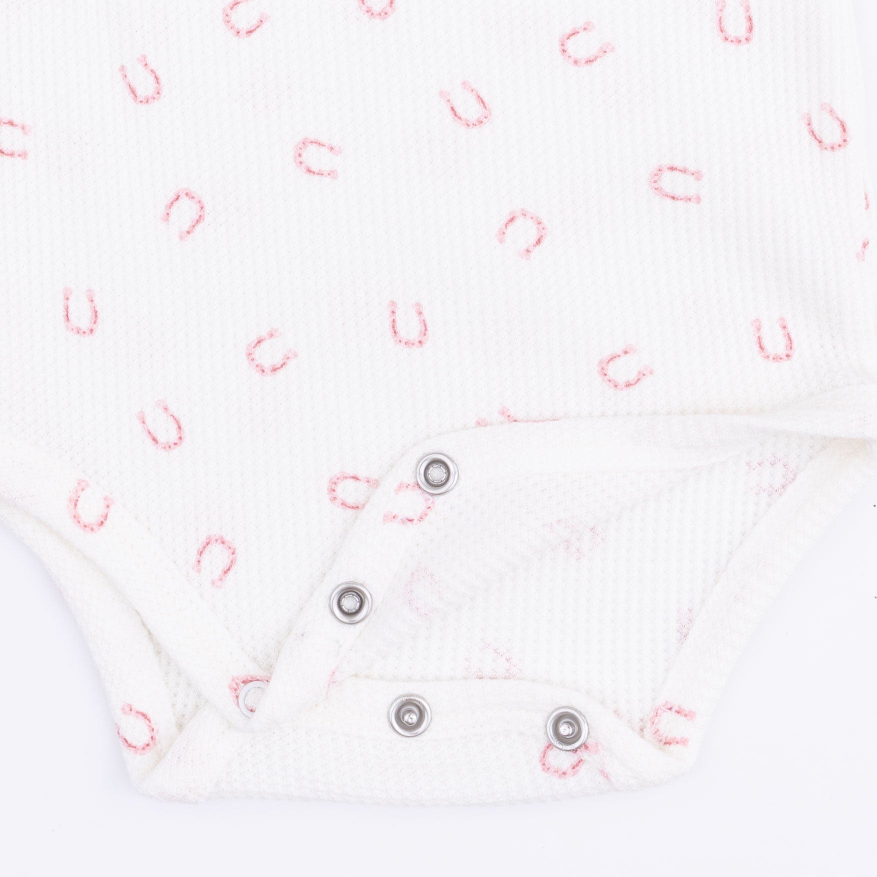Close-up of a textured white fabric with pink horseshoe pattern and metal snaps at the crotch.