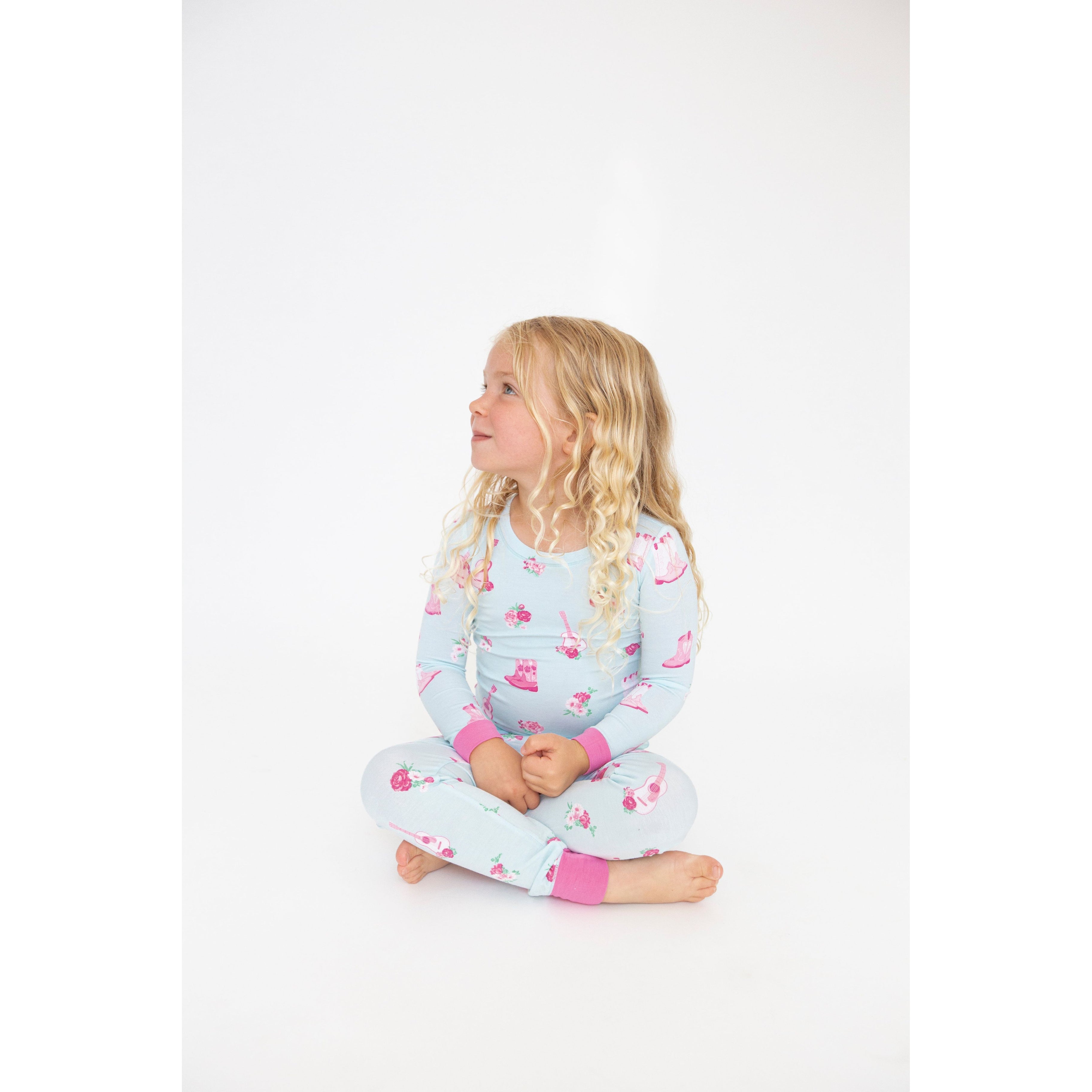 girl sitting and wearing blue two piece long sleeve loungewear set with pink fancy cowgirl print