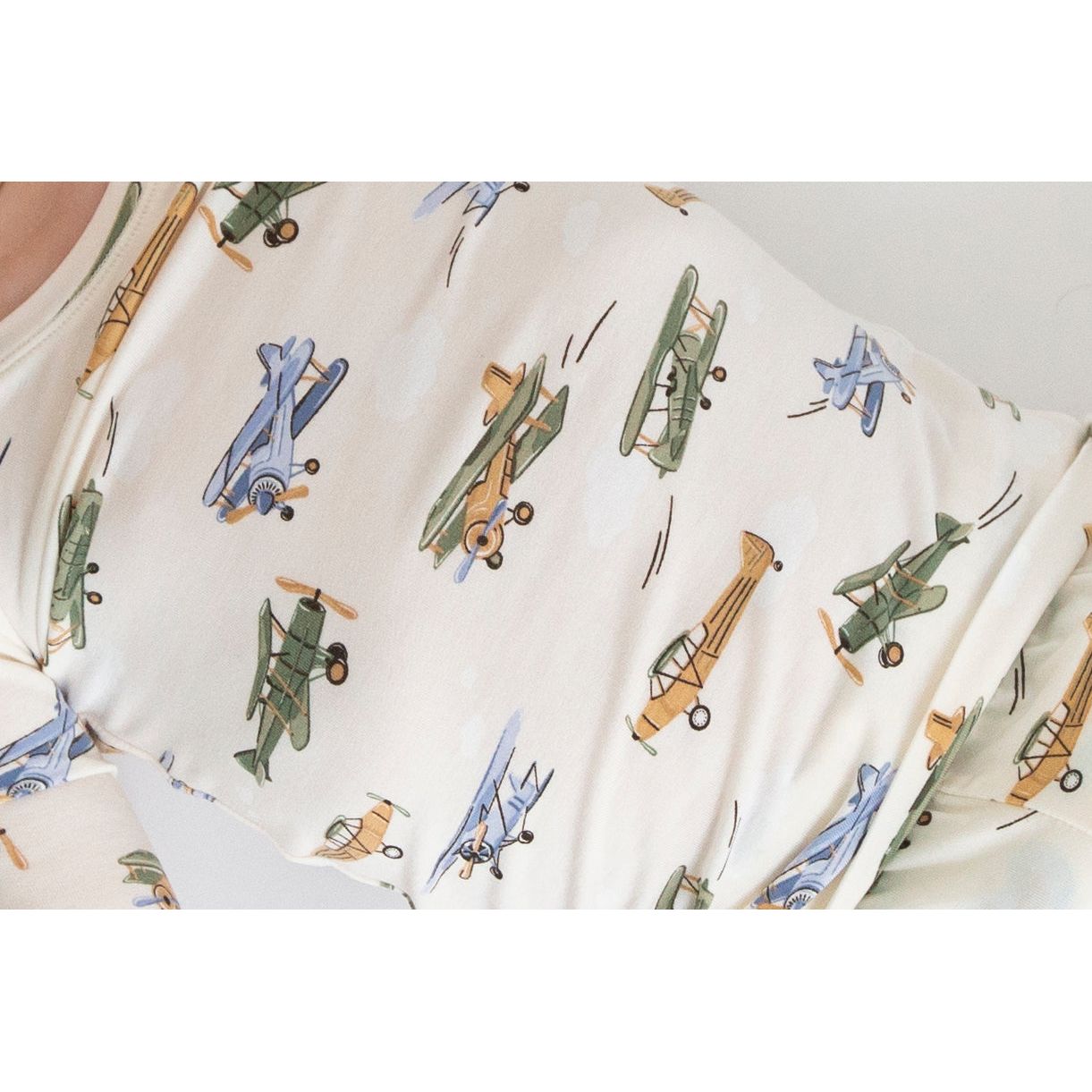 up close of toddler boy wearing off white lounge set with blue, green and tan vintage airplanes print and green on the wrists and ankles