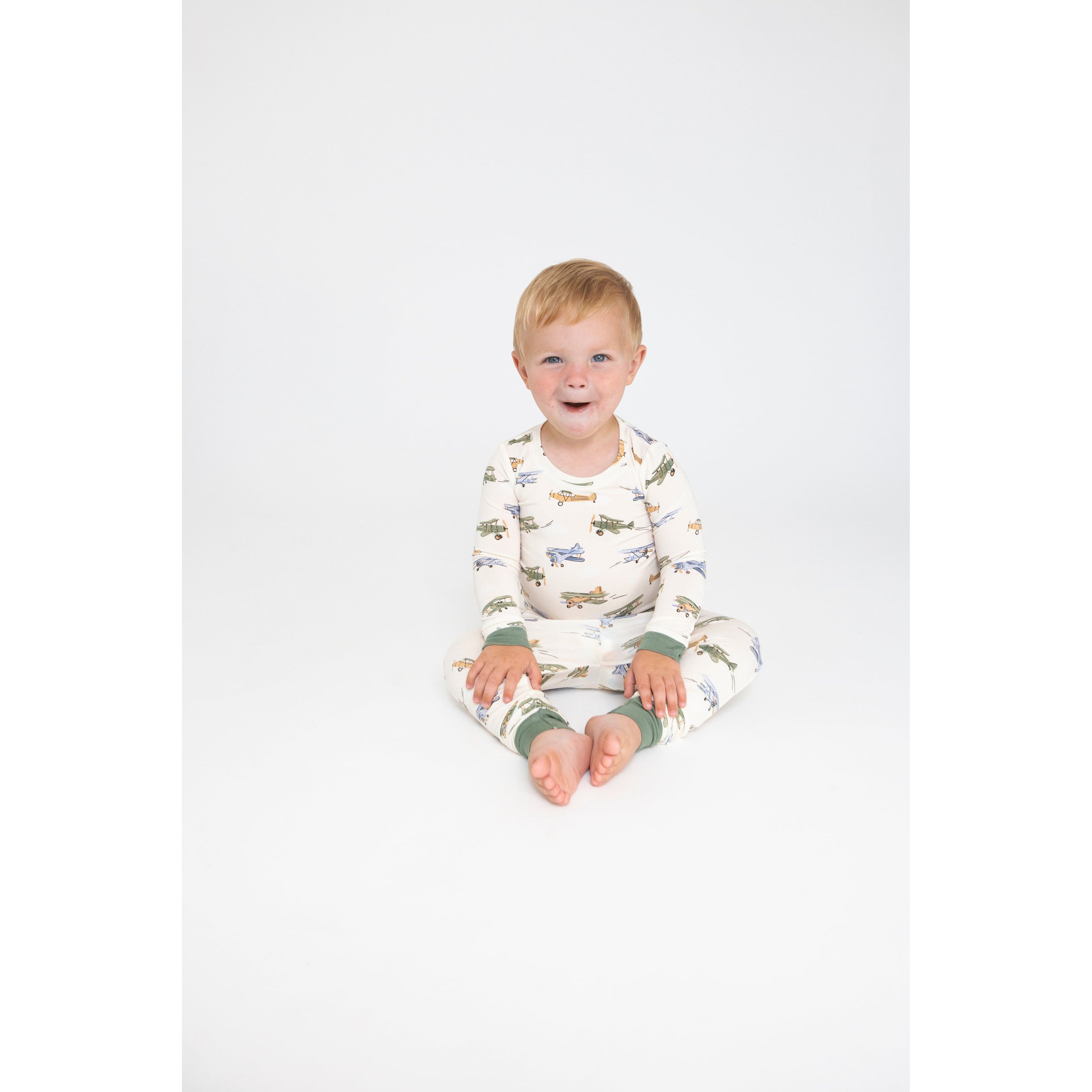 toddler boy wearing toddler boy wearing off white lounge set with blue, green and tan vintage airplanes print and green on the wrists and ankles