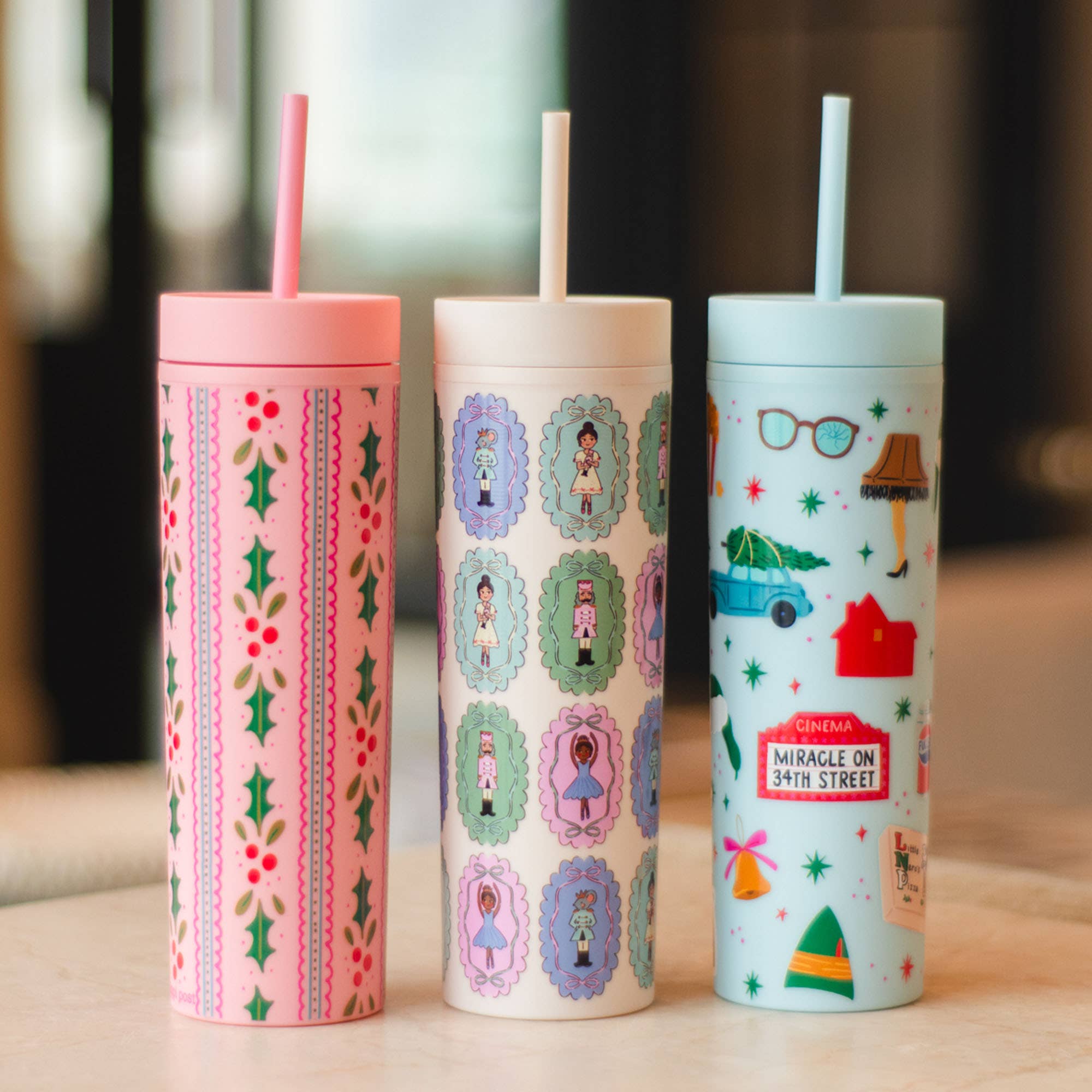 Three Pippi Post skinny acrylic tumblers with colorful holiday movie inspired artwork including floral patterns cinema signs houses and festive characters each with a straw