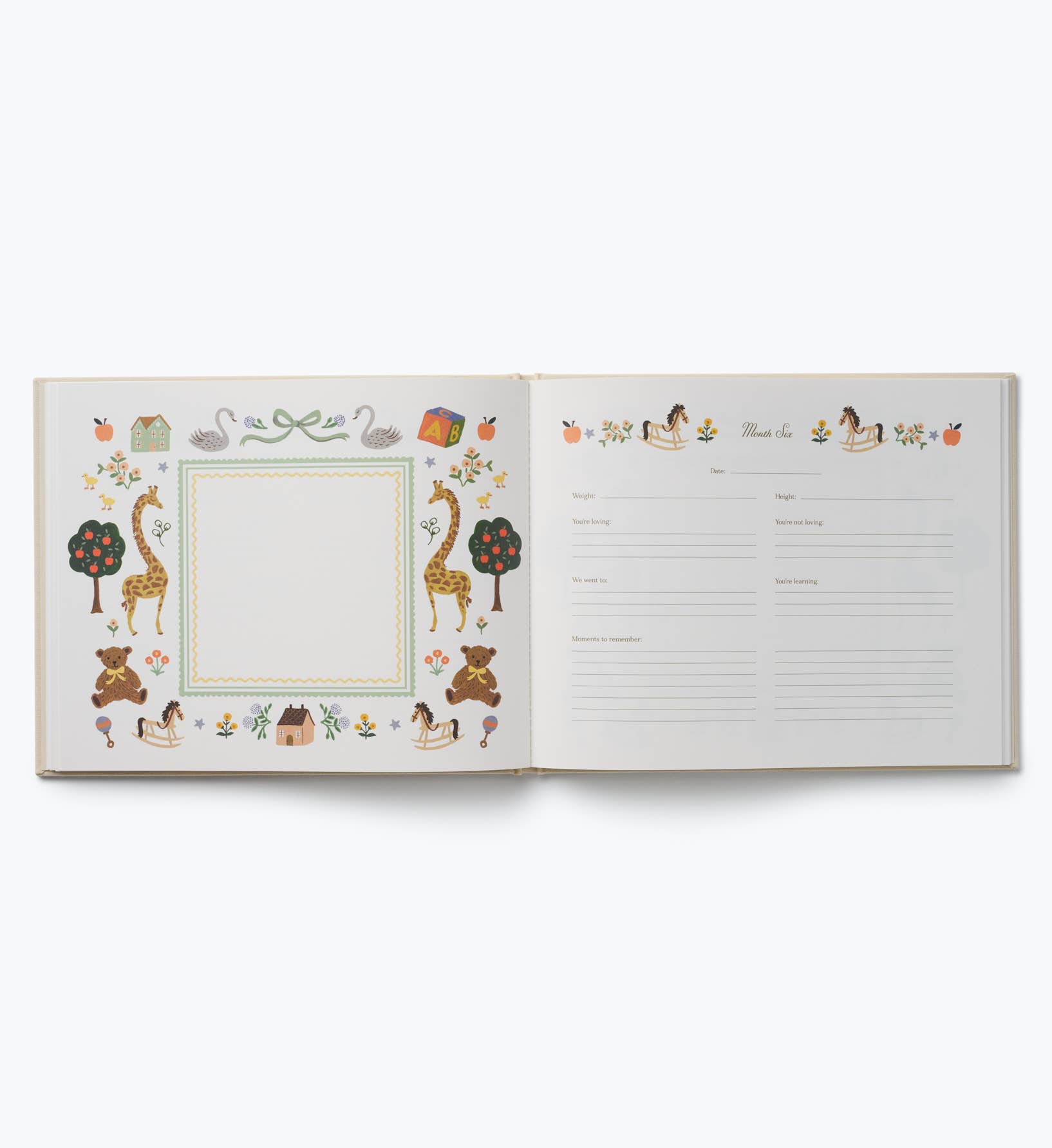 Open illustrated keepsake baby book by Rifle Paper Co. with a framed memory page on the left and milestone writing sections on the right