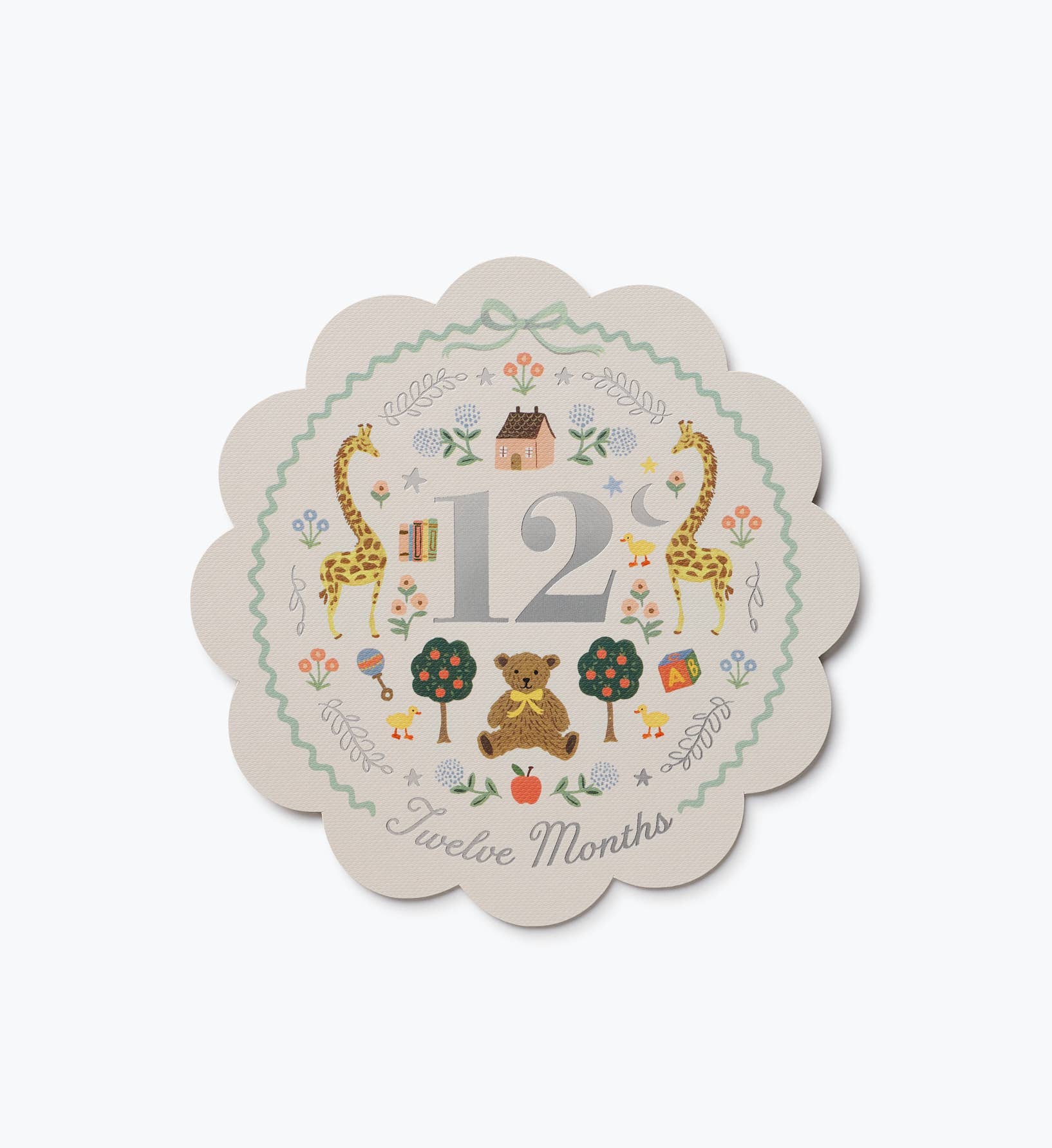 Illustrated twelve month baby milestone card with giraffes bears and floral details on a scalloped design by Rifle Paper Co.