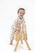 A toddler girl wearing a white short-sleeve pajama set with a pink and green golf pattern sits on a small wooden horse chair against a plain white background.