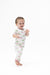 A smiling toddler standing barefoot on a seamless white background, wearing a white short-sleeve pajama romper with a pink and green golf print.