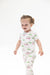 A toddler girl wearing a white short-sleeve footless pajama romper with a green and pink golf course and cart pattern, standing against a solid white background.