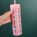 Pink 16 ounce skinny acrylic tumbler with straw held by hand and decorated with holly leaves red berries and scalloped stripes from Pippi Post