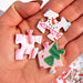 Three colorful pieces from a 500 piece Christmas jigsaw puzzle held in a hand featuring festive gingerbread village artwork by Pippi Post