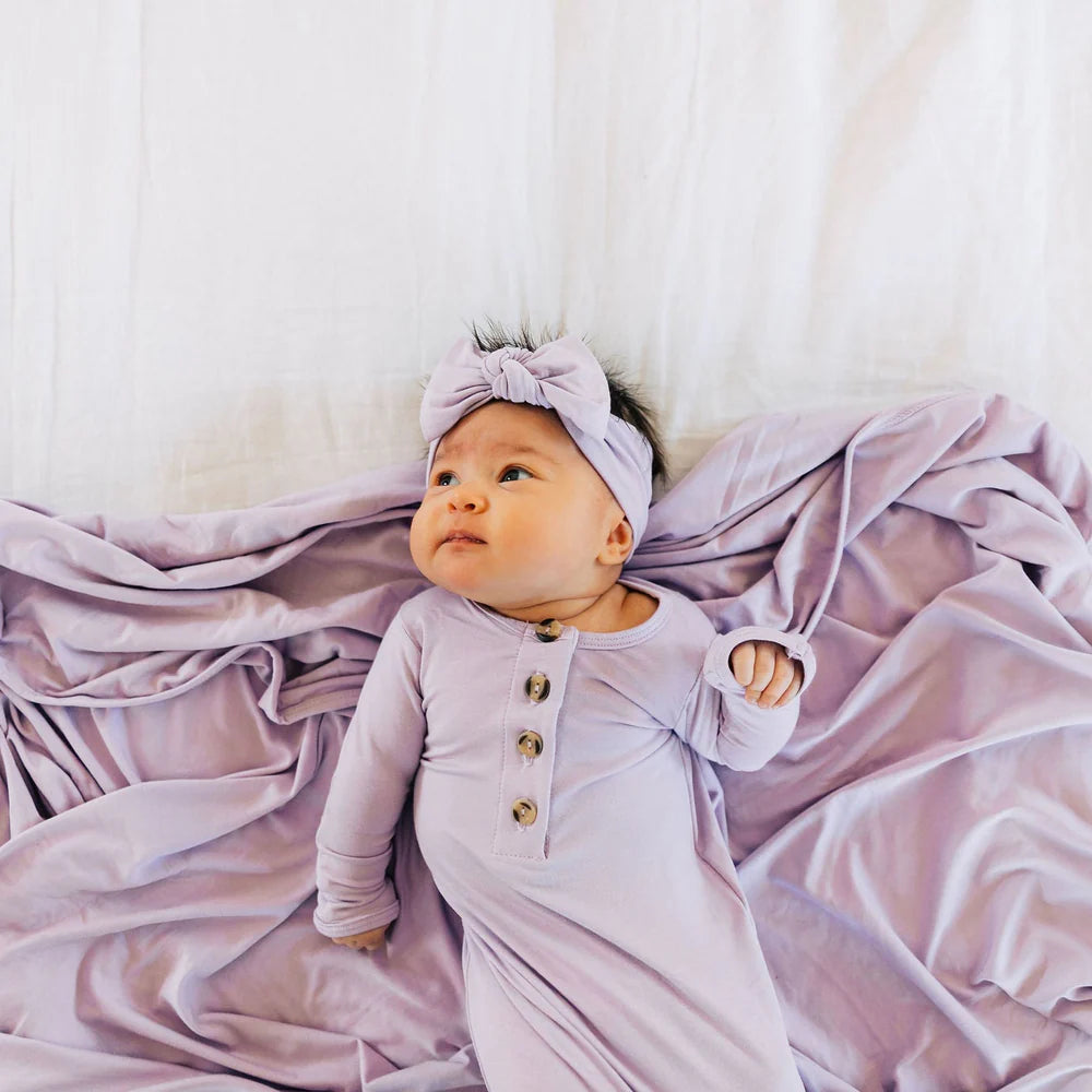 Baby in a light purple outfit and headband lying on a matching blanket.