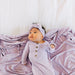 Baby in a light purple outfit and headband lying on a matching blanket.