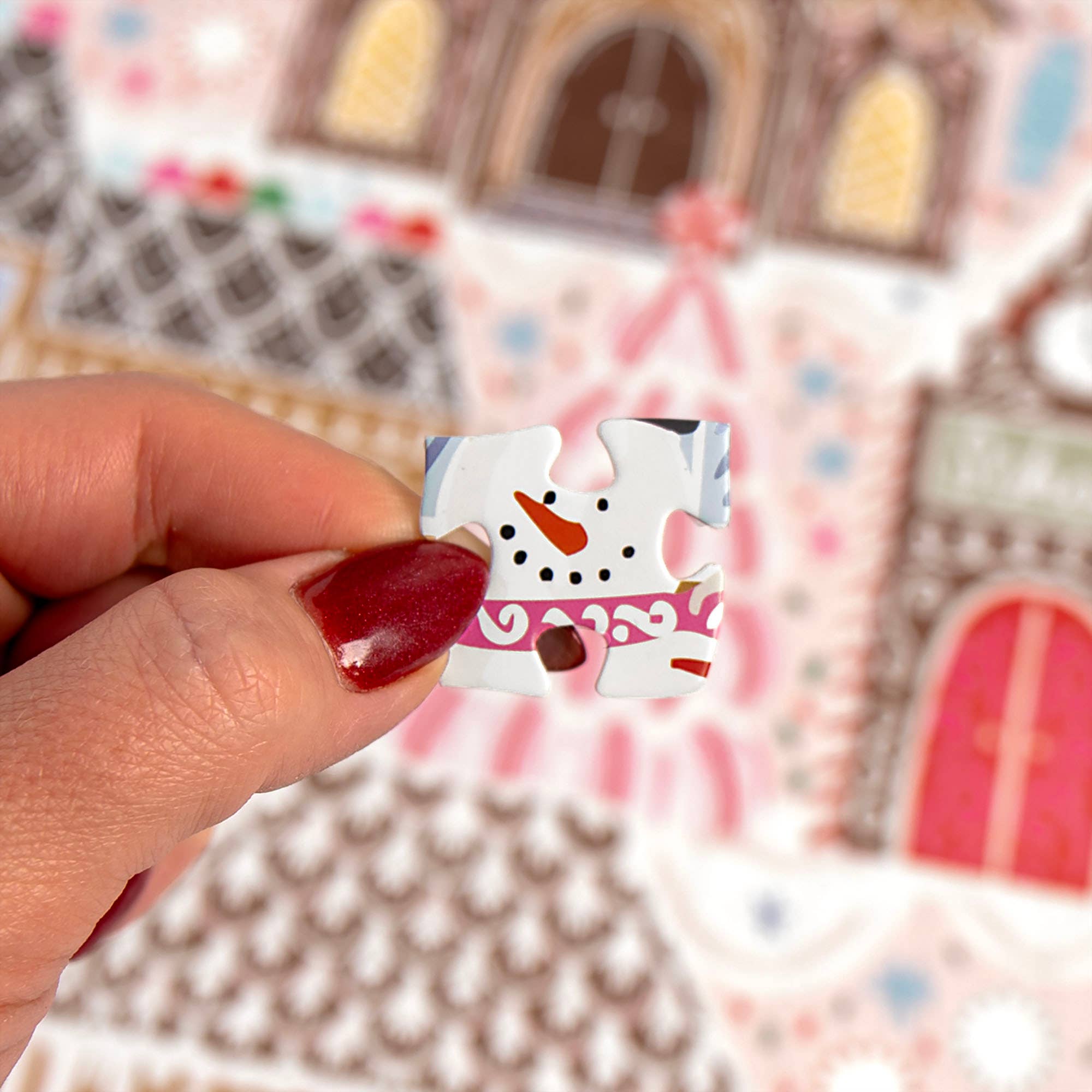 Close up of a hand holding a snowman puzzle piece over a colorful gingerbread village scene from the Pippi Post Christmas jigsaw puzzle