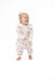 A baby girl wearing a two piece outfit with a pink and brown football print, standing barefoot against a solid white background.