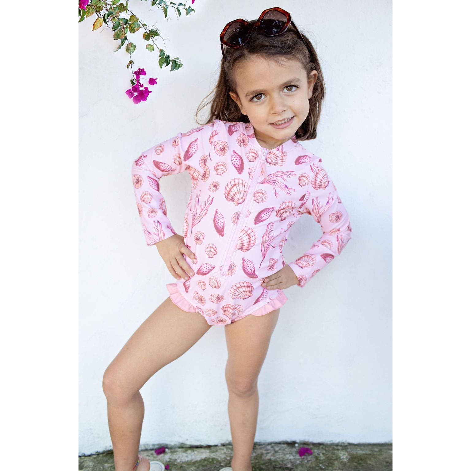 girl wearing light pink long sleeve rashguard swimsuit with pink seashell print and half zip in the center