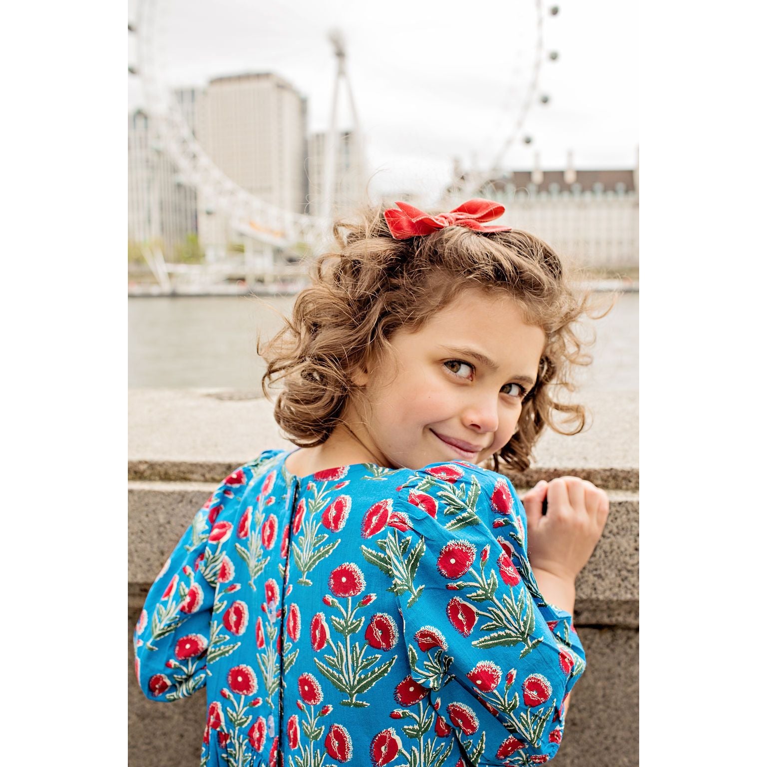 girl wearing blue 3/4 length sleeve dress with red poppy flower print