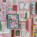 Pippi Post Gingerbread Square Christmas jigsaw puzzle box featuring a colorful gingerbread village scene surrounded by festive holiday stationery and gifts on a pink background