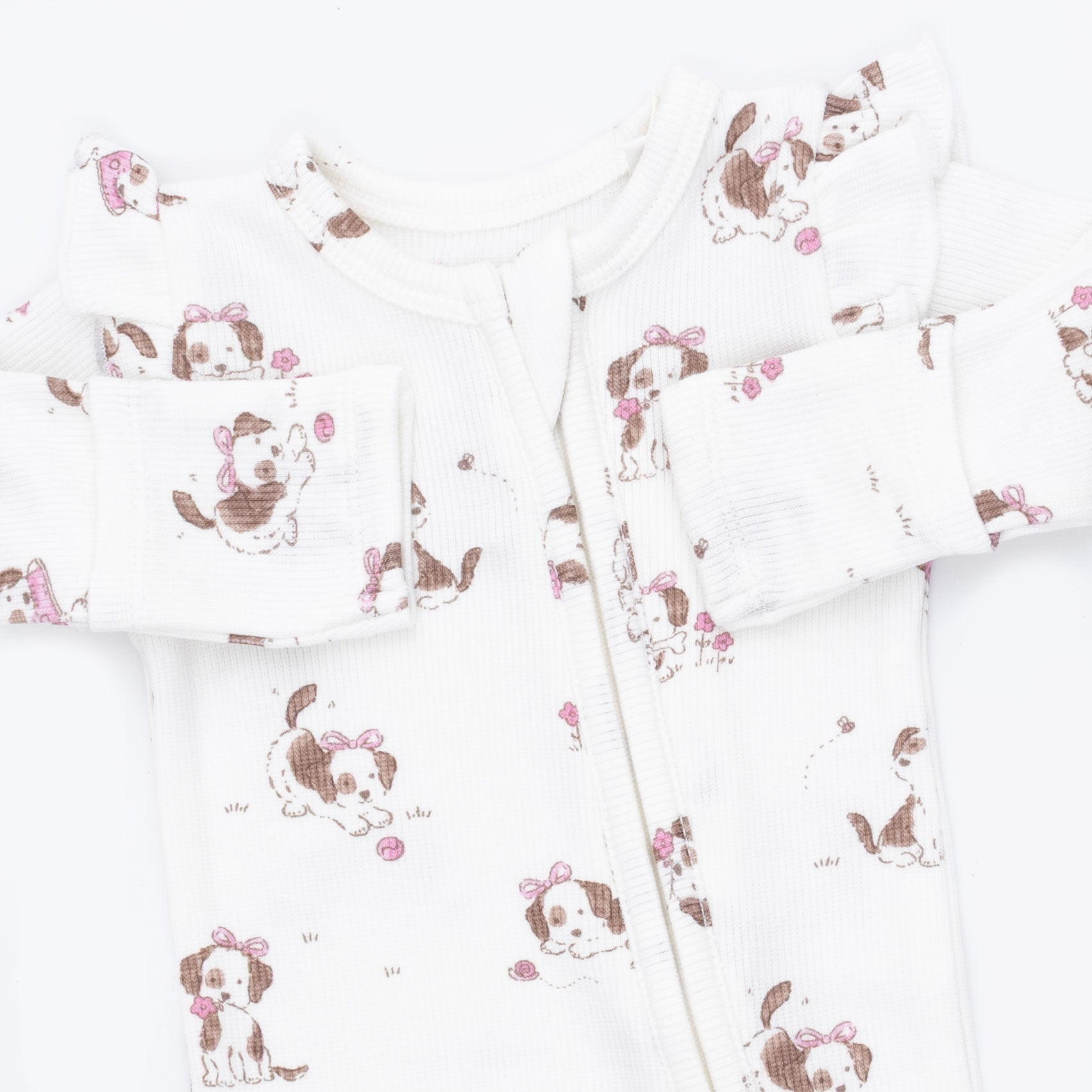 White long-sleeve baby footless sleeper with a front zipper and an all-over print of brown and white puppy illustrations wearing pink bows.