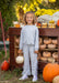 A young girl stands outdoors in front of a wooden crate filled with pumpkins, wearing a light blue-gray waffle-knit long-sleeve top and matching wide-leg pants with side tie details, paired with white sneakers.