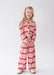 A young girl with blonde hair stands against a light gray studio background wearing a matching two-piece lounge set with a red and pink harlequin diamond pattern. The set includes a long-sleeve top and wide-leg pants.