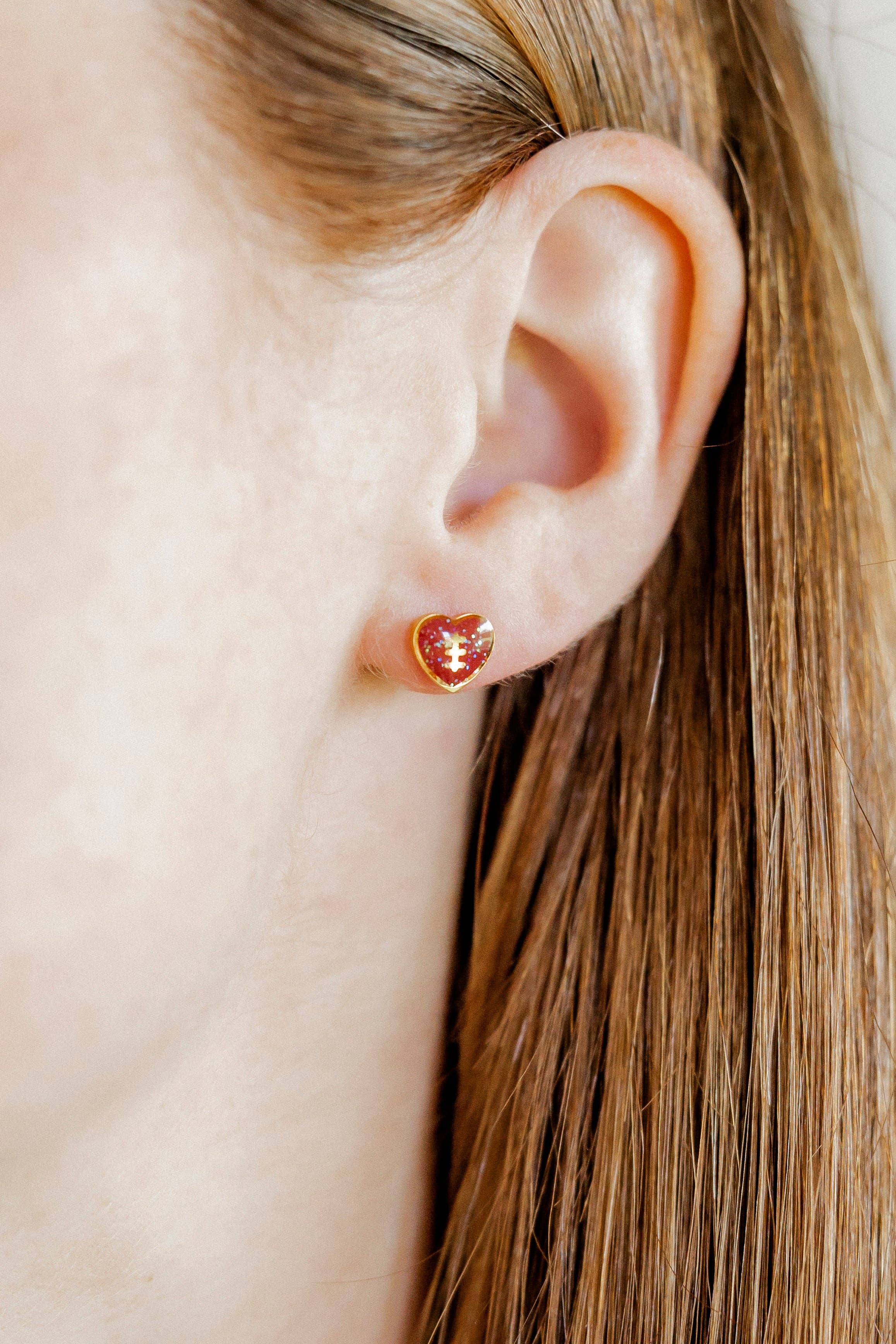 Football heart-shaped earrings worn by a person with long hair.