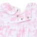 Close-up of a baby romper with pink and white toile pattern and button details.