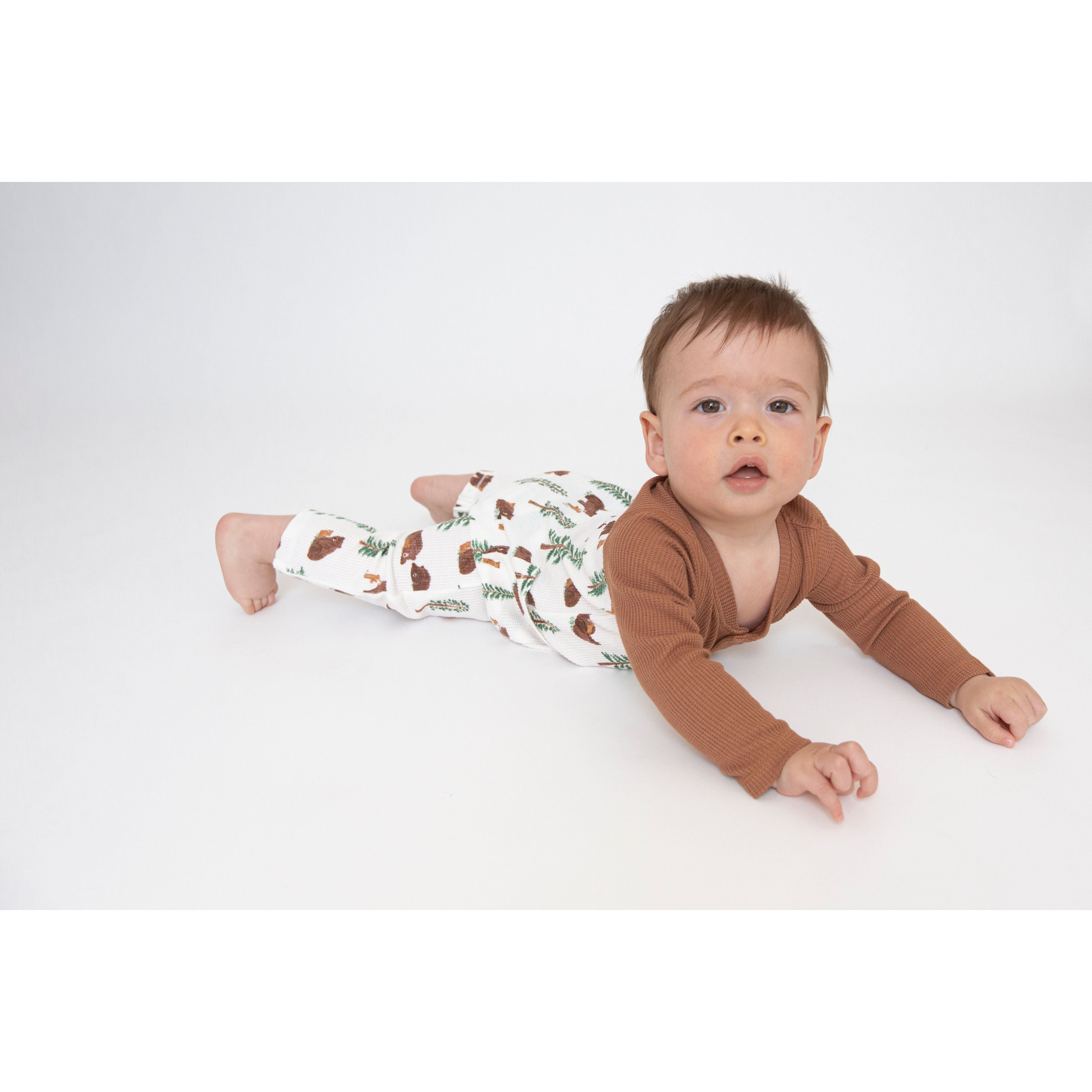 Baby wearing Romper with brown sleeves and collar with a white body with a bear and trees print