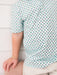 A close-up of a child wearing a white short-sleeve polo shirt with a repeating pattern of small green and black pumpkin faces, paired with light beige shorts against a white paneled wall.