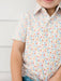 A close-up of a child wearing a short-sleeve button-up shirt with an all-over multicolor alphabet print on a white base, paired with blue jeans.
