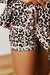 Close-up of a person wearing leopard-print shorts with a cream zipper detail, showing the fabric pattern and part of the body.