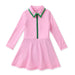 A pink long-sleeve tennis dress with a split neckline, featuring a green-trimmed collar and a green zipper detail down the front, displayed on a clean white background.