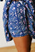 Close-up of a person wearing blue floral shorts with pink and white flowers, holding the side of the garment to show the fabric and drawstring waist.