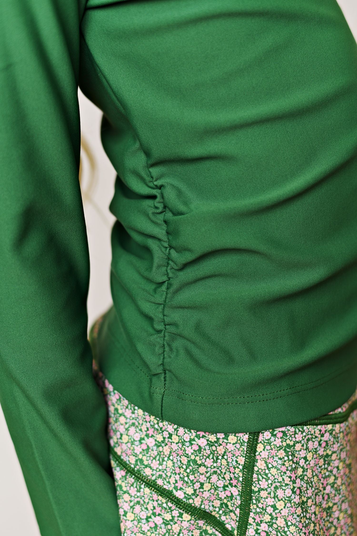 Close-up of a green long-sleeve ruched top paired with green floral-patterned bottoms, cropped to show the torso and waist area.