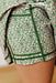 Close-up of a person wearing green floral shorts with dark green contrast stitching, showing the fabric pattern and leg detail.