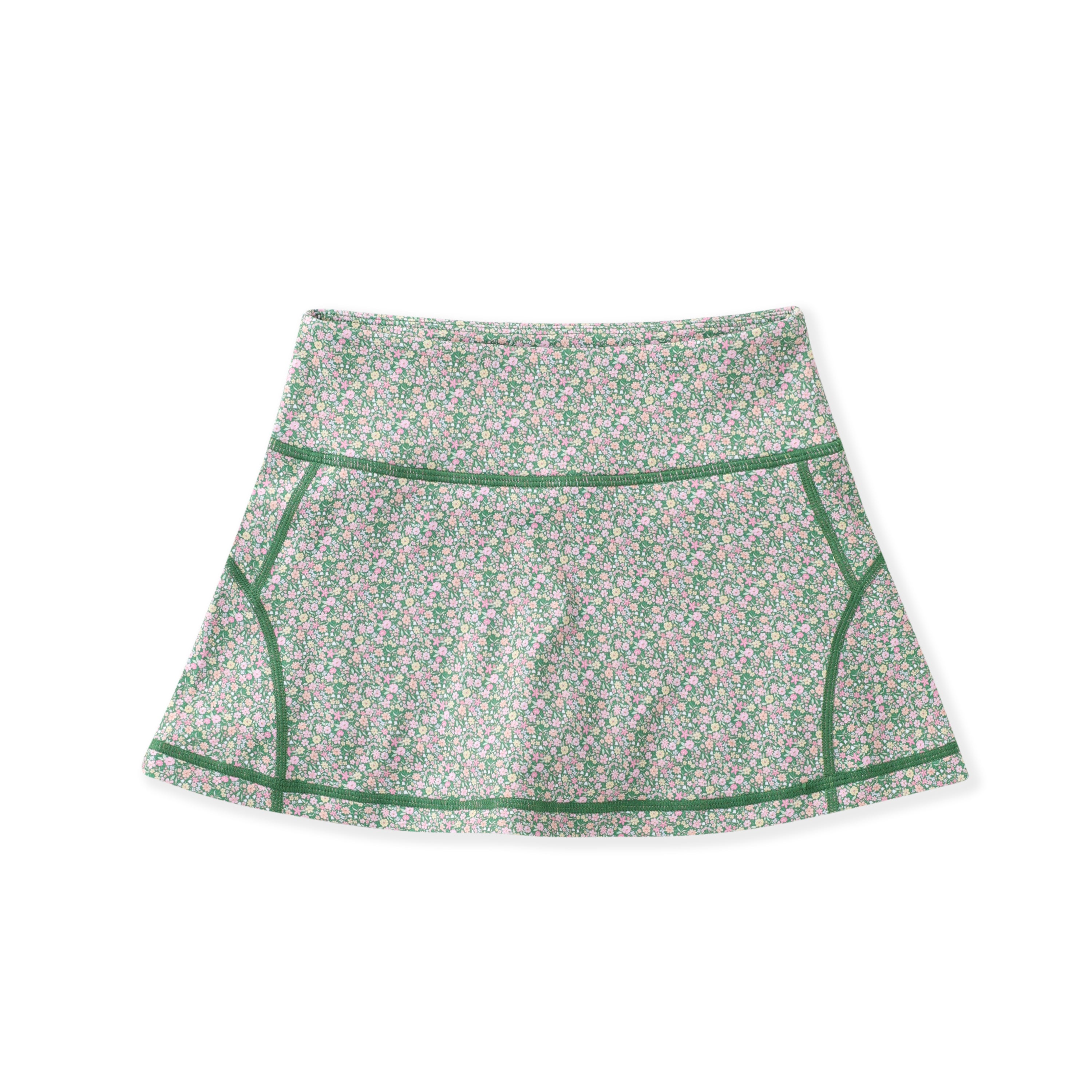 A high-waisted athletic skirt with a dense green, pink, and white floral pattern, featuring solid green contrast piping along the seams, displayed on a clean white background.