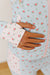 A close-up of a person wearing a light blue floral zip-up jacket with pink and green rose patterns, showing a hand resting on the front pocket.
