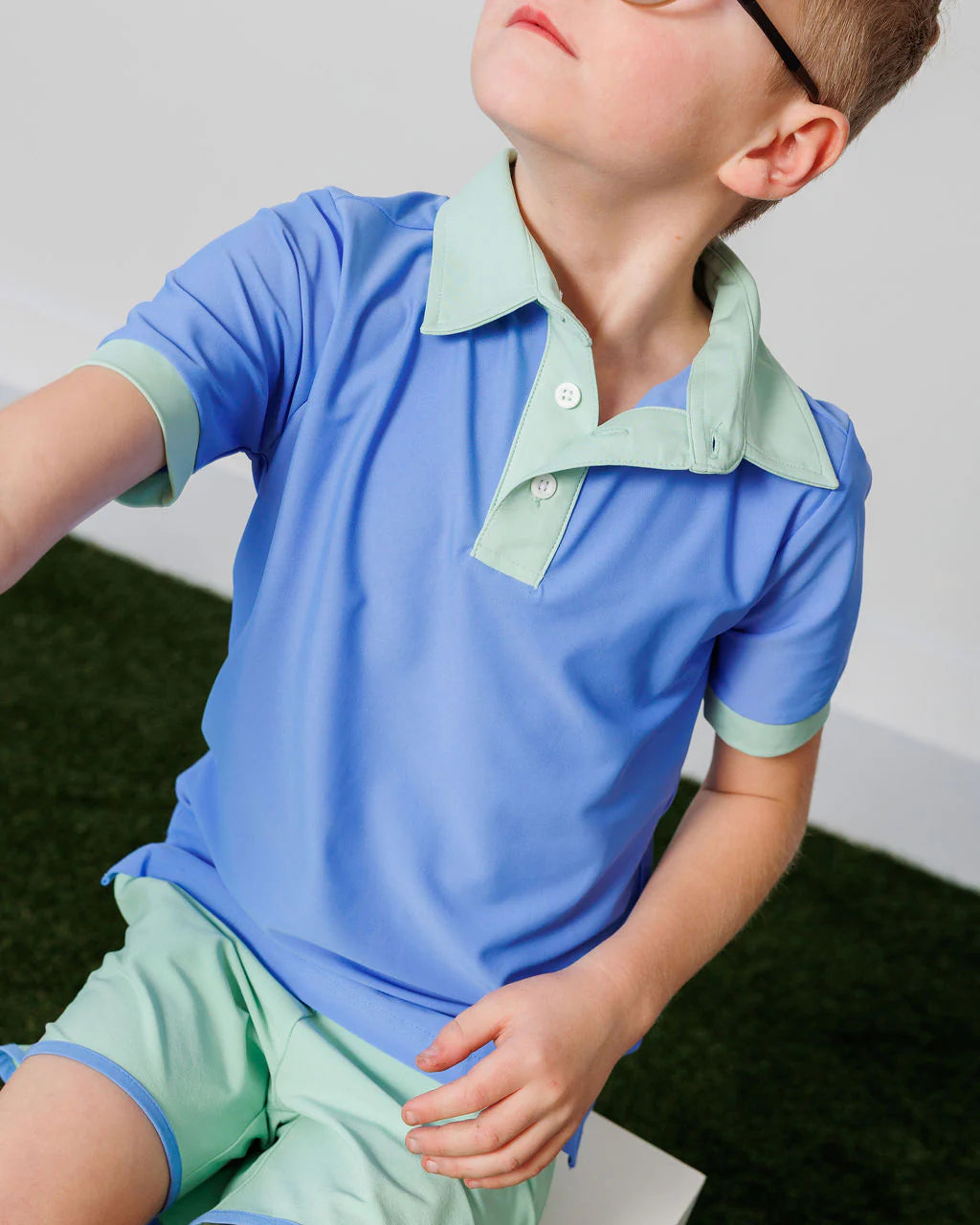 Child wearing a blue and green polo shirt with matching shorts on a grassy background