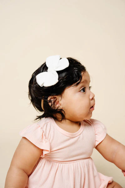 Child wearing a pink dress and white floral headband against a beige background