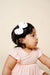 Child wearing a pink dress and white floral headband against a beige background