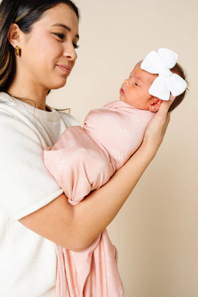 Woman holding a baby wrapped in pink fabric against a beige background