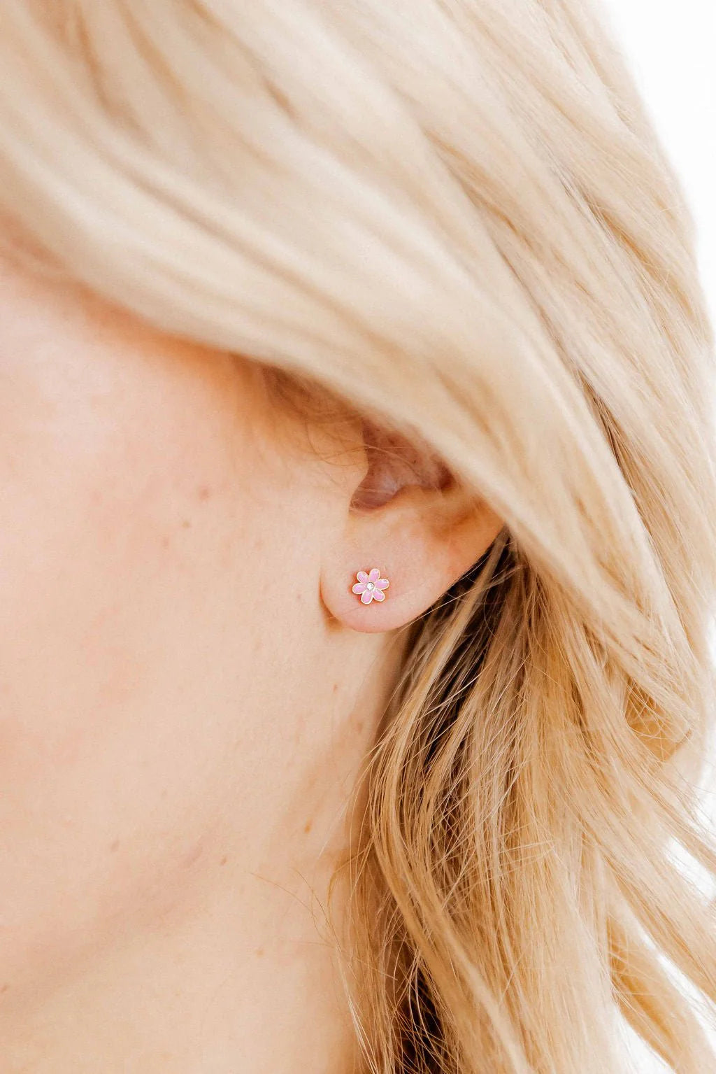 Close-up of a person wearing a small pink earring with a flower design.