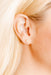 Close-up of an ear wearing a small gold flower earring with blonde hair.