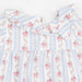 A close-up of a children's dress featuring a white base with light blue vertical stripes and a pink floral print, complete with a ruffled collar and snap buttons.
